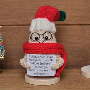 Op de afbeelding: Handgemaakte Holiday Cheer Potato-figuur met rode sjaal, muts en bril, met een bordje met de tekst "Christmas is magical with you in it!". Een kleine kerstboom en een houten sneeuwvlok zijn ook aanwezig.