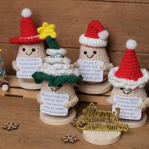 May include: A collection of crocheted potato figures, each with a unique Christmas-themed hat. One is a Christmas tree. Each potato holds a small sign with a message. A gold "Merry Christmas" sign and wooden snowflakes are also present.