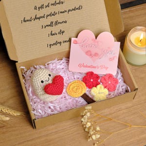 Puede incluir: Un juego de regalo de San Valentín en una caja de cartón, que incluye una patata en forma de corazón de ganchillo, pequeñas flores, una pinza para el pelo y una tarjeta de felicitación. La tarjeta dice "love you" y "Valentine's Day".