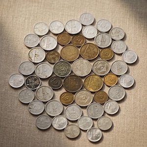 Pode incluir: Uma coleção de moedas antigas, dispostas em um padrão circular. As moedas, de vários tamanhos e cores, apresentam tons prateados e dourados. Algumas moedas exibem desenhos e símbolos intrincados.
