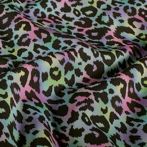Könnte beinhalten: Stoff mit einem farbenfrohen Leopardenmuster. Das Design zeigt schwarze Flecken auf einem Hintergrund aus Pastellfarben, darunter Rosa, Lila, Grün und Blau. Der Stoff ist gefaltet, wodurch die Textur und die Musterunterschiede sichtbar werden.