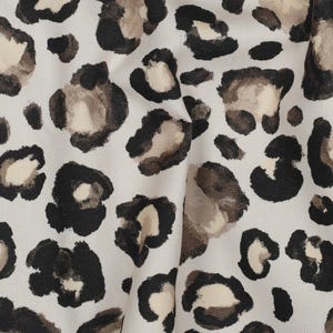 Könnte beinhalten: Nahaufnahme eines Stoffes mit Leopardenmuster. Das Muster zeigt schwarze, braune und beige Flecken auf einem hellbeigen Hintergrund. Der Stoff hat ein leicht strukturiertes Aussehen.