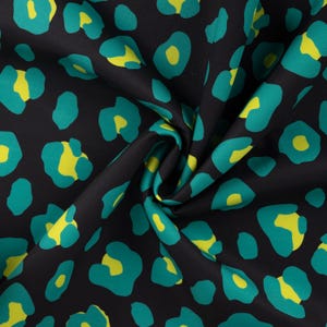 Könnte beinhalten: Schwarzer Stoff mit einem sich wiederholenden Leopardenmuster in Türkis und Gelb. Der Stoff ist gefaltet, wodurch Schatten und Texturen entstehen. Die Flecken sind unterschiedlich groß und geformt, mit gelben Zentren.