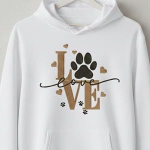 May include: White hooded sweatshirt with a front pocket. The design features the word "love" with a paw print replacing the "o". Small paw prints and hearts are scattered around the word. The letters are a tan color.