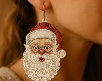 May include: Embroidered Santa Claus earrings. The earrings feature a red hat, white beard, and round glasses. The Santa face is detailed with a red nose and rosy cheeks. The earrings are attached to a silver-colored hook.
