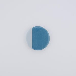 Puede incluir: Un botón redondo bicolor con un diseño dividido. Un lado es azul claro y el otro es azul más oscuro. El botón tiene una superficie ligeramente texturizada y una estética simple y minimalista. Diámetro aproximado de 2,5 cm.