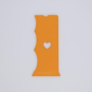May include: Orange phone case with a heart-shaped cutout. The case has a unique, wavy edge design on one side and the text "smashed it" at the bottom. The case is designed to fit a smartphone.