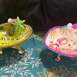 May include: A white ceramic mug with a black handle and the text "But First, Coffee" in a bold, black font. The mug is set against a blurred background, suggesting a cozy setting.