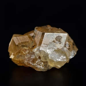 Pu&ograve; includere: Un gruppo di cristalli color marrone dorato con forme geometriche nette. I cristalli hanno una qualit&agrave; traslucida, con alcune aree che appaiono pi&ugrave; opache. Lo sfondo &egrave; nero pieno, evidenziando la bellezza naturale del minerale.