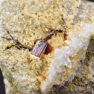 May include: Close-up of a mineral specimen featuring a reddish-brown crystal formation embedded in a matrix of beige and white crystalline material. The crystals have a metallic luster, and the overall texture is rough and uneven.