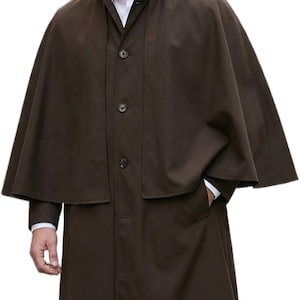 May include: A dark brown full-length coat featuring a cape-style overlay, a high stand-up collar, and a front button closure. The garment is worn over a white collared shirt, showcasing a structured silhouette with long sleeves and side pockets.