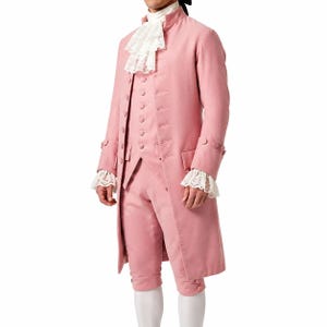 May include: A dusty pink long coat, matching vest, and knee-length breeches set. The ensemble features a white lace jabot at the neck and matching lace cuffs at the sleeves. The coat and vest are secured with rows of fabric-covered buttons.