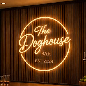 Può includere: Un'insegna al neon circolare con luce gialla calda montata su una parete a listelli di legno scuro. L'insegna mostra il testo The Doghouse BAR EST 2024 in un carattere corsivo stilizzato e sans-serif. L'ambiente include un bancone e bottiglie.