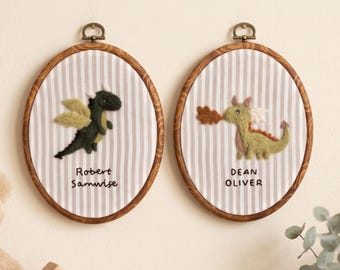 May include: Two oval wooden embroidery hoops containing fabric with vertical white and beige stripes. Each hoop features a felt dragon appliqué and embroidered names: Robert Samwise on the left and Dean Oliver on the right.