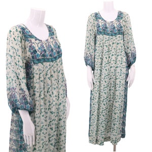Puede incluir: Un vestido maxi blanco con estampado floral en tonos azules y verdes. El vestido tiene mangas largas con puños fruncidos y un escote redondo. El vestido está hecho de una tela ligera y tiene una silueta fluida.