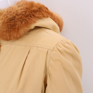 May include: A beige hooded jacket with a brown fur collar. The jacket has a long sleeve and a fitted silhouette.