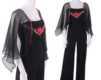 Puede incluir: Mono negro con un diseño de flor bordada en rojo, verde y blanco en el corpiño. El mono tiene piernas anchas y una capa negra transparente con un diseño de flor bordada a juego.
