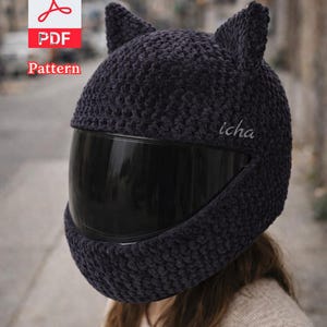 Puede incluir: Una funda de casco de motocicleta de ganchillo gris oscuro con orejas de gato y una visera negra. El texto "icha" está en el lateral de la funda del casco. La imagen también incluye un icono de patrón PDF.