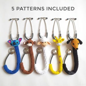 Peut inclure: Cinq housses de stéthoscope crochetées en forme d'animaux sont présentées sur un fond blanc. Les animaux comprennent un extraterrestre bleu, un singe marron, un mouton blanc, une girafe jaune et un chien noir et marron. Le texte "5 PATTERNS INCLUDED" est en haut.