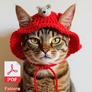 May include: A tabby cat wearing a bright red crocheted hat with a small gray mouse on top. The hat is tied with a red cord. A PDF pattern icon is in the lower left corner.