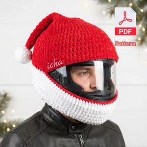 Könnte beinhalten: Ein rot-weißer gehäkelter Weihnachtsmannhut, der für einen Motorradhelm entworfen wurde. Der Hut hat eine rote Oberseite, einen weißen Rand und eine weiße Bommel. Das Wort "icha" ist auf den Hut gestickt. Ein PDF-Muster ist verfügbar.