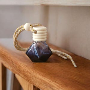 May include: A dark purple glass bottle with a white and gold stopper and a string hanging from it. The bottle is sitting on a wooden shelf.