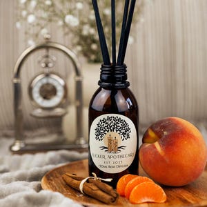 May include: A brown glass bottle with a black label that reads "Flicker Apothecary Est 2025 100ml Reed Diffuser". The bottle is filled with a clear liquid and has black reeds sticking out of the top. The bottle is sitting on a wooden surface with a peach, cinnamon sticks, and orange slices.
