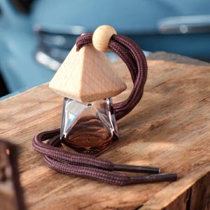 May include: A brown wooden and glass car air freshener with a brown cord. The air freshener is shaped like a pyramid and has a clear glass bottle with a brown liquid inside.