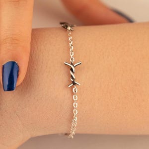 May include: A silver bracelet featuring a barbed wire charm. The bracelet is worn on a person's wrist.