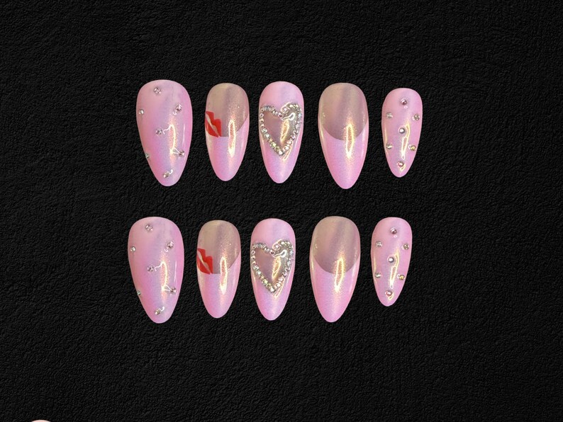 May include: Set of ten pink press-on nails. Some nails feature silver rhinestones, a silver heart design, or a red lip design. The nails have an iridescent finish and are arranged on a black surface.