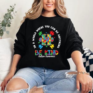 May include: Black sweatshirt with a colorful puzzle piece design and the text "In a world where you can be anything be kind Autism Awareness".