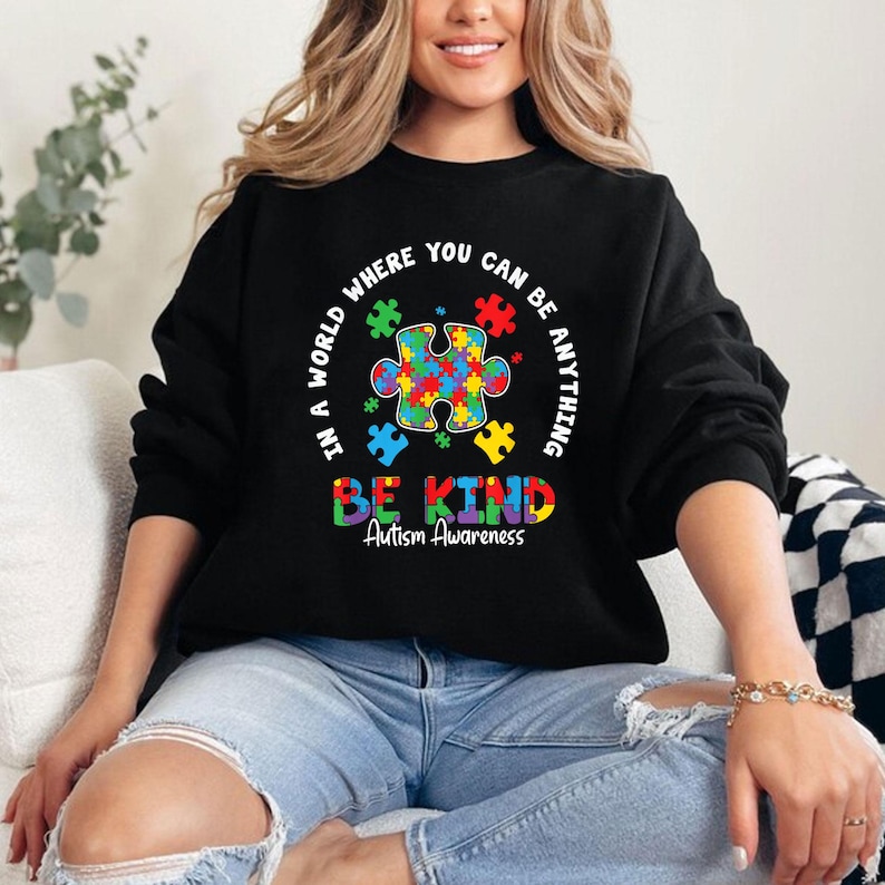 May include: Black sweatshirt with a colorful puzzle piece design and the text "In a world where you can be anything be kind Autism Awareness".