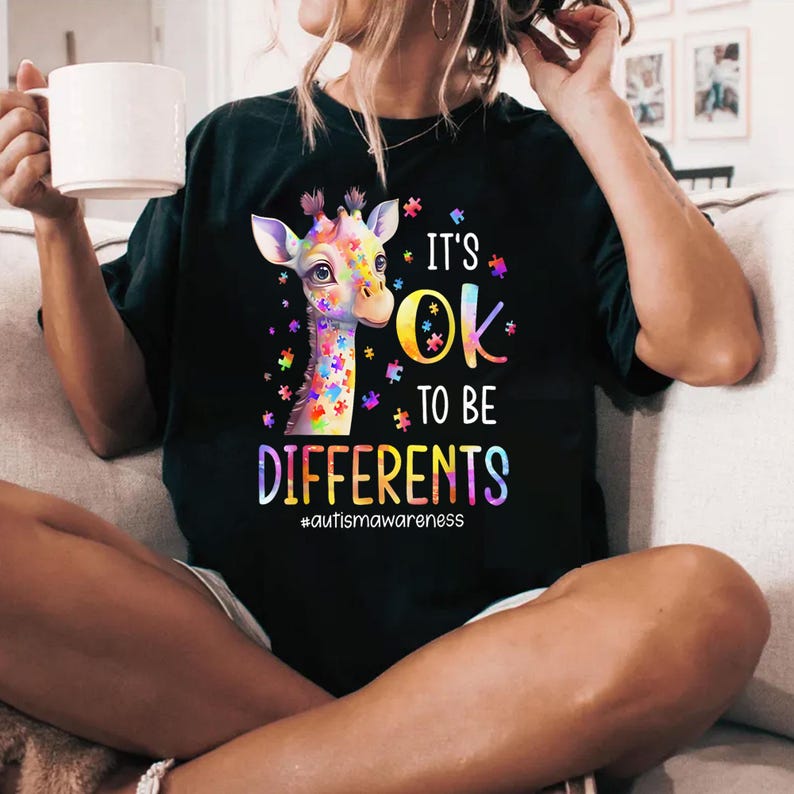 May include: Black t-shirt with a colorful giraffe made of puzzle pieces. The text "It's Ok To Be Differents #autismawareness" is printed on the shirt.