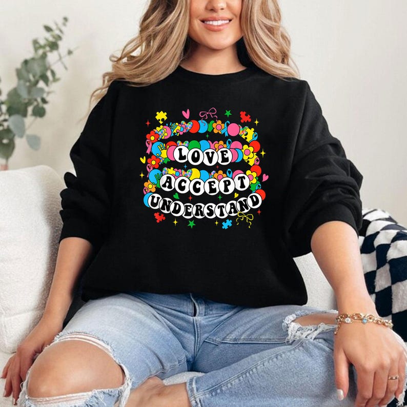 May include: Black sweatshirt with a colorful graphic design that says "Love Accept Understand" surrounded by flowers, hearts, and stars.