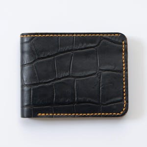 May include: A black leather wallet with a crocodile pattern and yellow stitching.