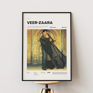 Op de afbeelding: Een ingelijste filmposter voor Veer-Zaara met een centrale afbeelding van twee mensen die elkaar omhelzen voor een gouden boog. De poster bevat de titel Veer-Zaara in vetgedrukte zwarte letters bovenaan, samen met productiedetails.