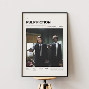May include: A framed movie poster for Pulp Fiction featuring a central photograph of two men in black suits holding handguns. The poster has a white border with black text including the title, director Quentin Tarantino, and film details.