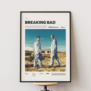 Pode incluir: Pôster emoldurado com o título "BREAKING BAD" em letras pretas. A imagem mostra dois homens de macacão branco em uma paisagem desértica, com uma autocaravana. O pôster tem um design minimalista com texto e blocos de cores.