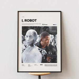 Puede incluir: Póster de película enmarcado para "I, Robot" con un robot futurista y un hombre sosteniendo un arma. El póster tiene un marco negro y está montado en una pared blanca. El título y los créditos están en la parte superior.