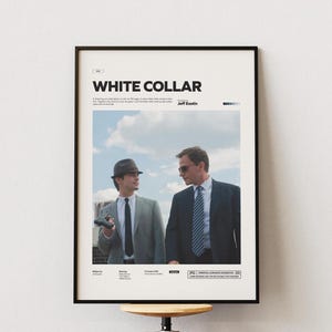 Op de afbeelding: Een ingelijste poster met de titel "WHITE COLLAR" in witte letters. De afbeelding toont twee mannen in pakken, een met een pistool, tegen een bewolkte lucht. De poster zit in een zwarte lijst.