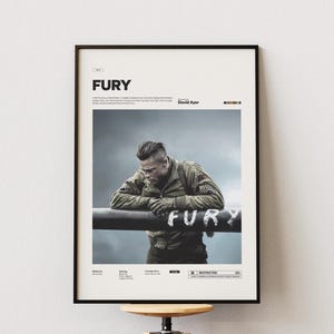 Könnte beinhalten: Gerahmtes Filmplakat für "Fury", das einen Mann in Militäruniform zeigt, der sich auf eine Oberfläche mit dem Wort "FURY" lehnt. Das Poster hat einen schwarzen Rahmen und ist an einer weißen Wand ausgestellt.