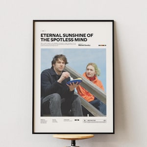 Puede incluir: Póster enmarcado de la película "Eternal Sunshine of the Spotless Mind". El póster tiene un marco negro y muestra una fotografía de dos personas. El hombre lleva una chaqueta negra y la mujer una chaqueta naranja. El póster incluye el título de la película y el nombre del director.