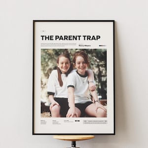 Könnte beinhalten: Gerahmtes Filmplakat für "The Parent Trap" mit zwei jungen Frauen in weißen T-Shirts und schwarzen Shorts. Das Poster hat einen schwarzen Rahmen und enthält Filmtitel, Credits und Bewertungsinformationen. Der Hintergrund ist eine hellfarbige Wand.