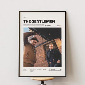 May include: Framed movie poster for "The Gentlemen" with two men in a scene. The poster has a black frame and features the film's title in white text at the top. The image shows a man in a brown jacket and another in a black coat.