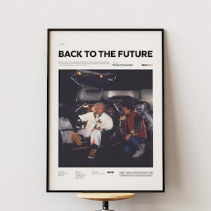 Könnte beinhalten: Gerahmtes Poster mit dem Film "Zurück in die Zukunft". Das Poster hat einen schwarzen Rahmen und zeigt eine Szene mit zwei Charakteren und einem DeLorean-Auto. Titel und Credits befinden sich oben, mit zusätzlichem Text unten.