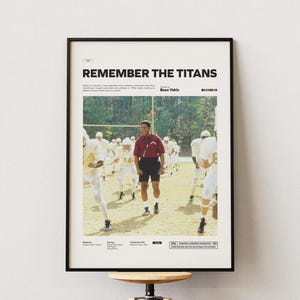 Puede incluir: Un póster enmarcado de la película "Remember the Titans" con una escena de un equipo de fútbol en un campo. El póster tiene un marco negro e incluye el título de la película, créditos y una clasificación PG.