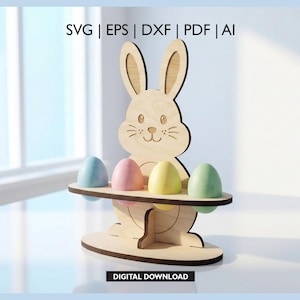 Op de afbeelding: Houten paashaasvormige eierhouder met vier pastelkleurige eieren. Het konijn heeft een lachend gezicht en houdt de eieren op een plank. De afbeelding bevat ook de tekst "SVG | EPS | DXF | PDF | AI" en "DIGITALE DOWNLOAD".