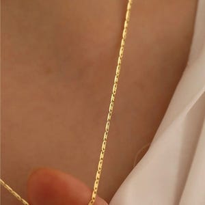 May include: A gold chain necklace with a delicate, thin design. The chain is made of small, oval-shaped links.