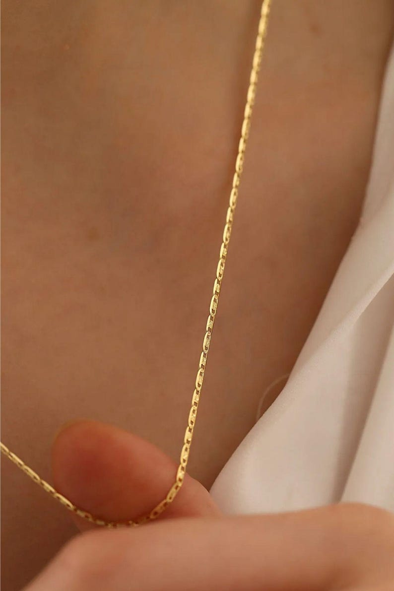 May include: A gold chain necklace with a delicate, thin design. The chain is made of small, oval-shaped links.