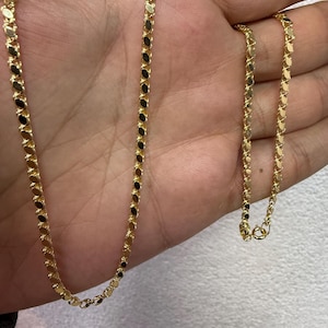 May include: A gold-colored chain necklace with a delicate, repeating oval link design. The necklace is displayed on a hand, showcasing its length and the intricate pattern of the links. The clasp is visible at the end of the chain.